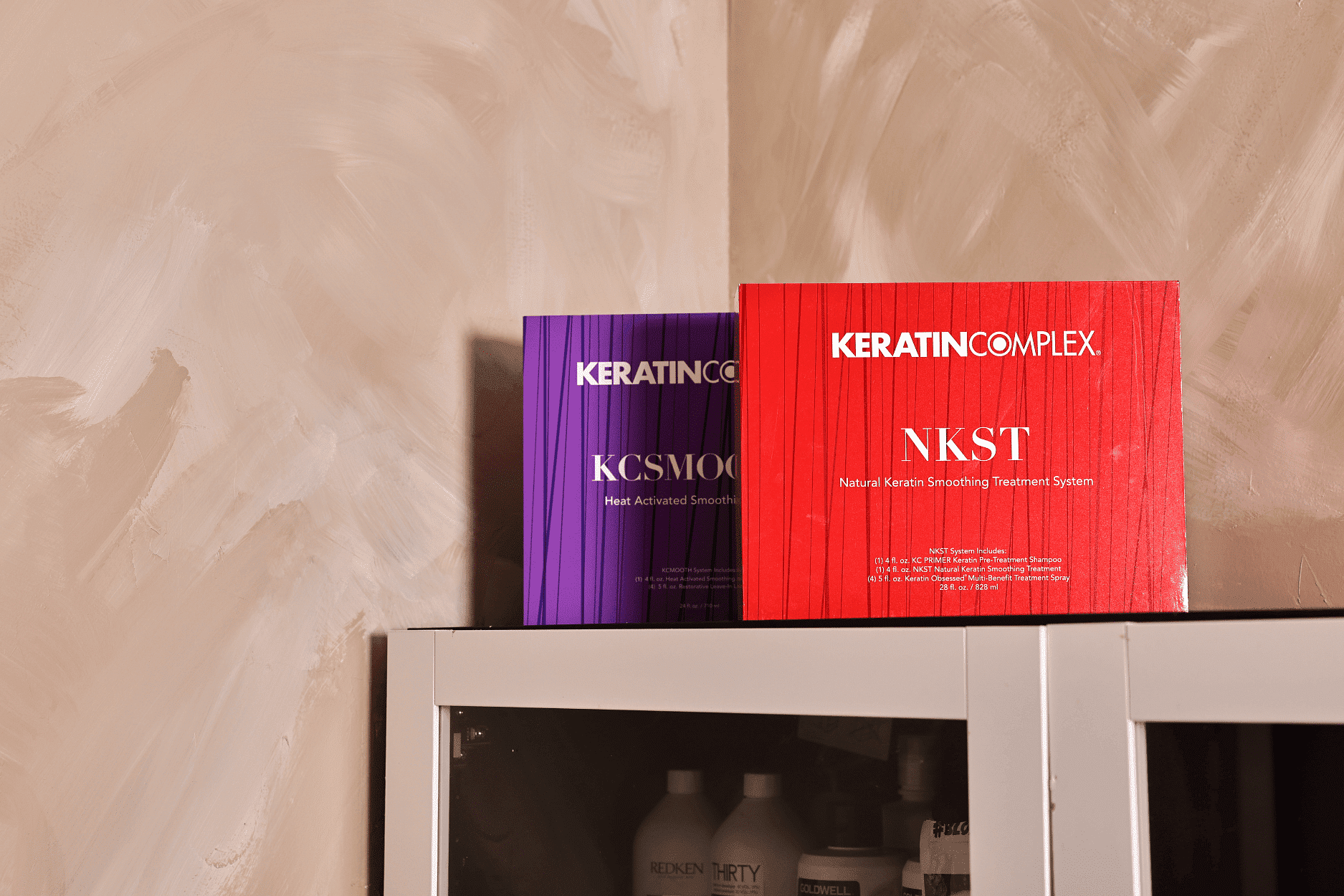 Keratin treatment products, KCSMOOTH (purple) and NKST (red), displayed on a cabinet shelf.